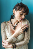 Woman wearing a beige lace dress with black jewelry against a teal background
