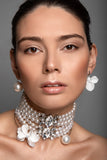 A close-up portrait of a woman wearing Sildare jewelry pearl choker necklace with white flower accents and matching pearl drop earrings against a neutral gray background.