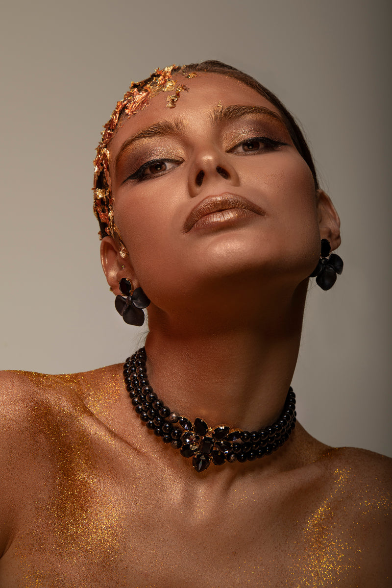 A three-strand black onyx beaded 24 carat gold plated Sildare Jewelry choker necklace with a central black crystal floral cluster and gold-tone clasp ends, shown on a plain white background.