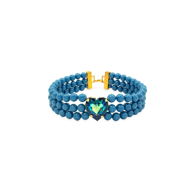 A blue pearl multi-strand beaded choker necklace in a medium blue color, featuring a gold-plated clasp and a central heart-shaped blue-green crystal, shown on a plain white background.