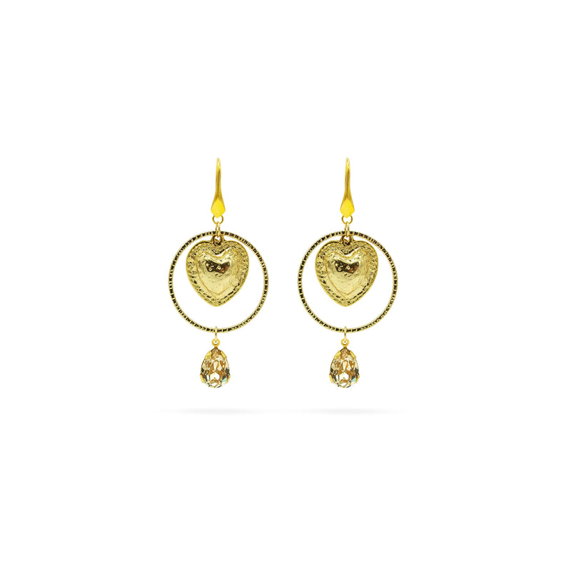 A pair of gold drop earrings featuring a textured heart-shaped charm inside a circular frame, with a small teardrop crystal pendant hanging below, set against a plain white background.